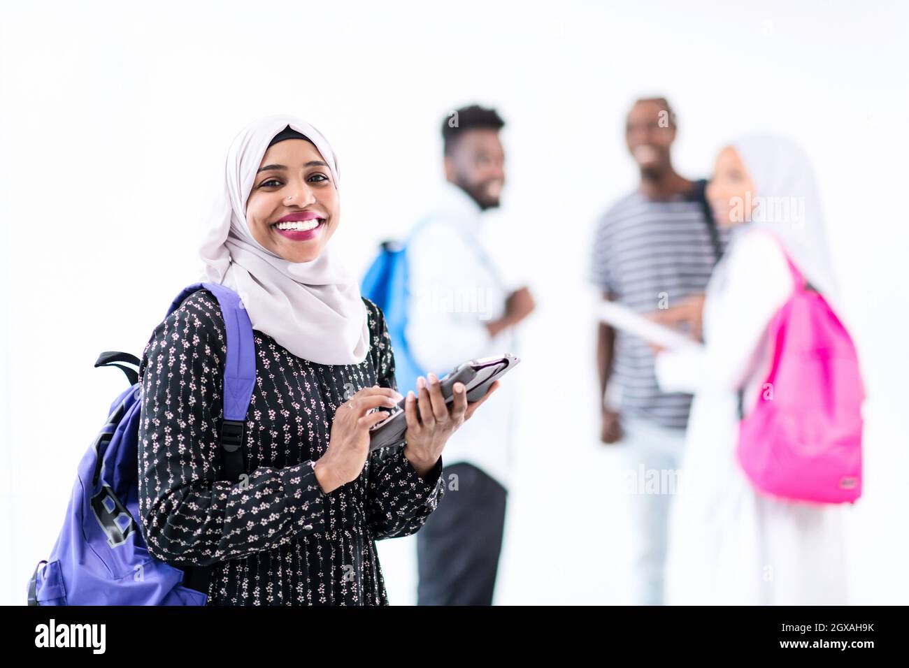 Giovani Musulmani moderni femmina africana studente utilizzando computer tablet con un gruppo di amici in background indossando il tradizionale hijab islamico vestiti Foto Stock