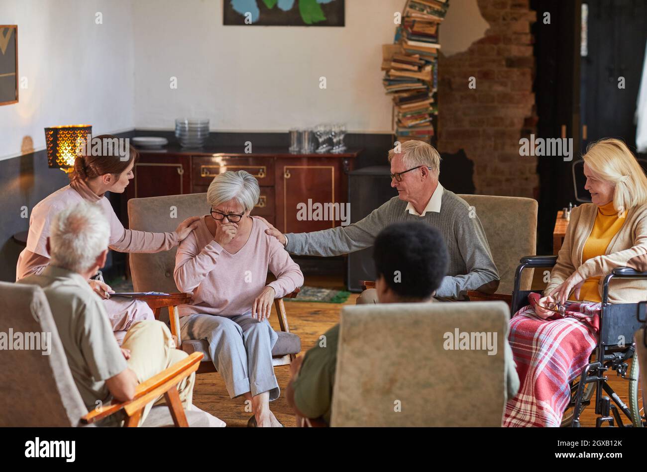 Gruppo di persone anziane sedute in cerchio durante la sessione di terapia a casa di pensionamento, concentrarsi sulla donna piangendo, spazio copia Foto Stock