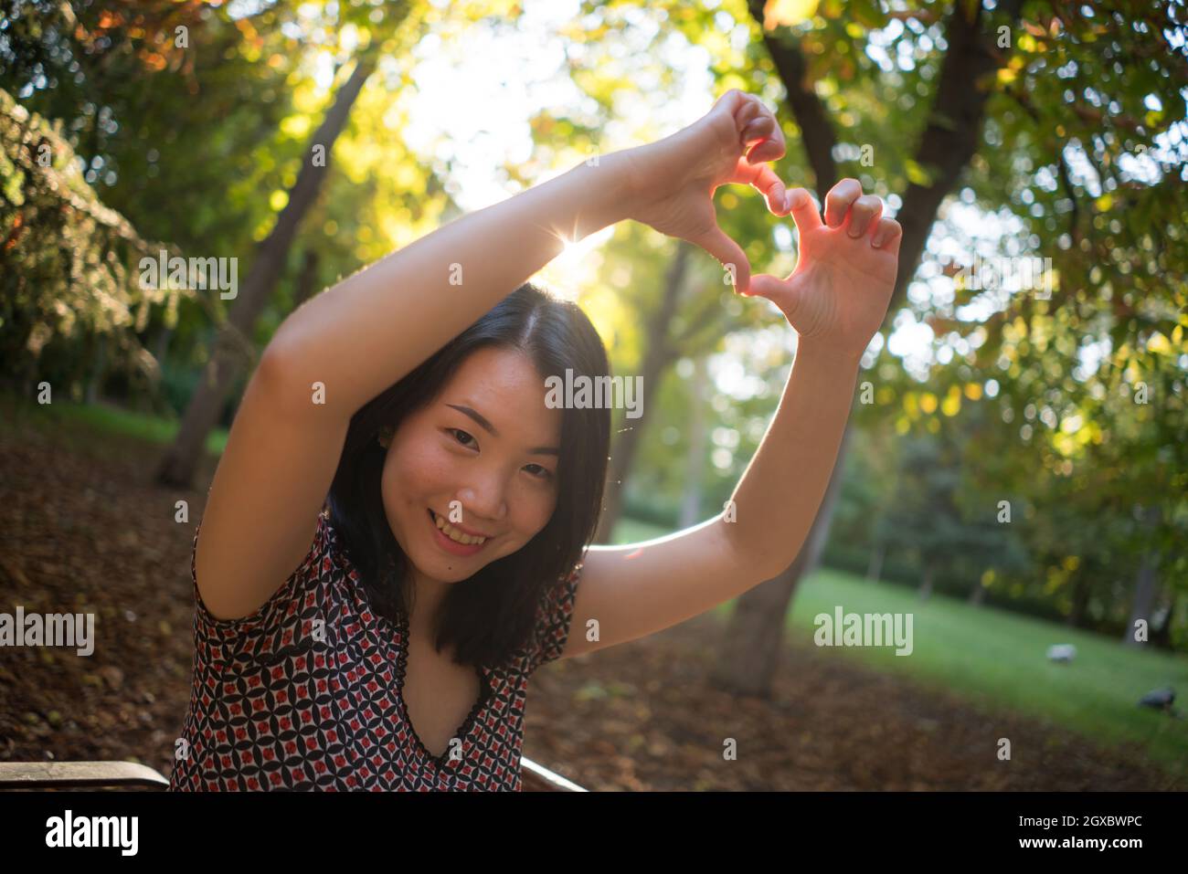 Outdoor lifestyle ritratto di giovane felice e bella donna asiatica cinese godendo rilassato e allegro al parco della città in autunno facendo amore cuore sha Foto Stock