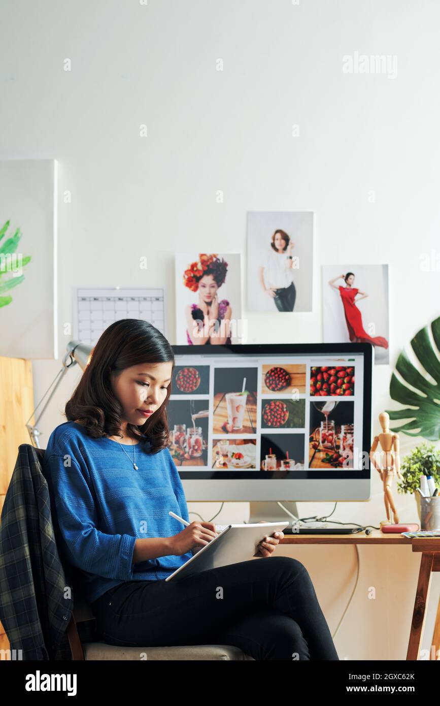 Concentrata giovane donna asiatica seduta al computer moderno e la creazione di design con digitalizzatore Foto Stock