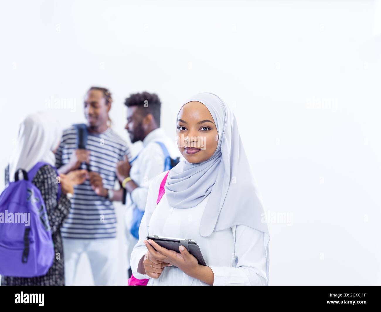 Giovane africana moderna donna musulmana studente utilizzando computer tablet con un gruppo di amici in background indossando il tradizionale hijab islamico vestiti Foto Stock