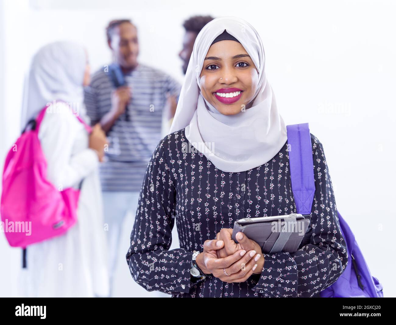 Giovane africana moderna donna musulmana studente utilizzando computer tablet con un gruppo di amici in background indossando il tradizionale hijab islamico vestiti Foto Stock