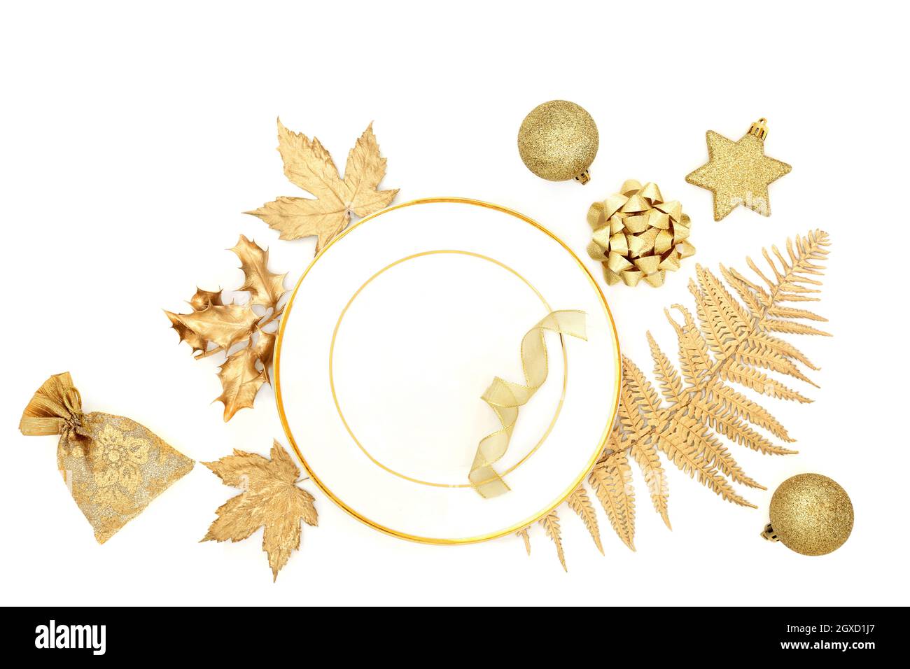 Oro natalizio festoso e tavola bianca con piatto, foglie, albero bauble decorazioni e regalo. Design decorativo per la stagione delle vacanze. Foto Stock