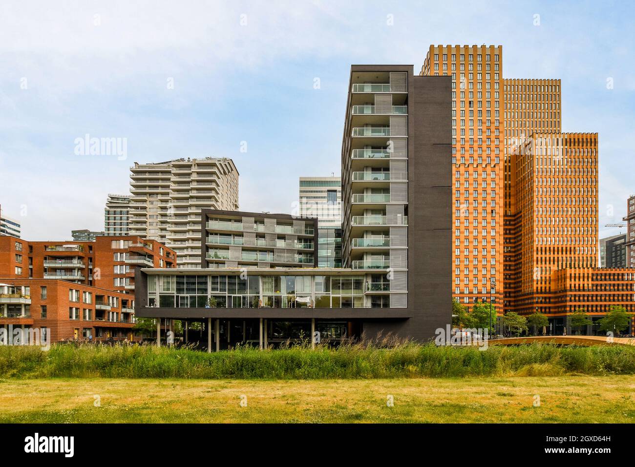 Edificio alto e moderno che si affaccia sul marciapiede con alberi e fiume sotto il cielo nuvoloso di Amsterdam Holland Foto Stock