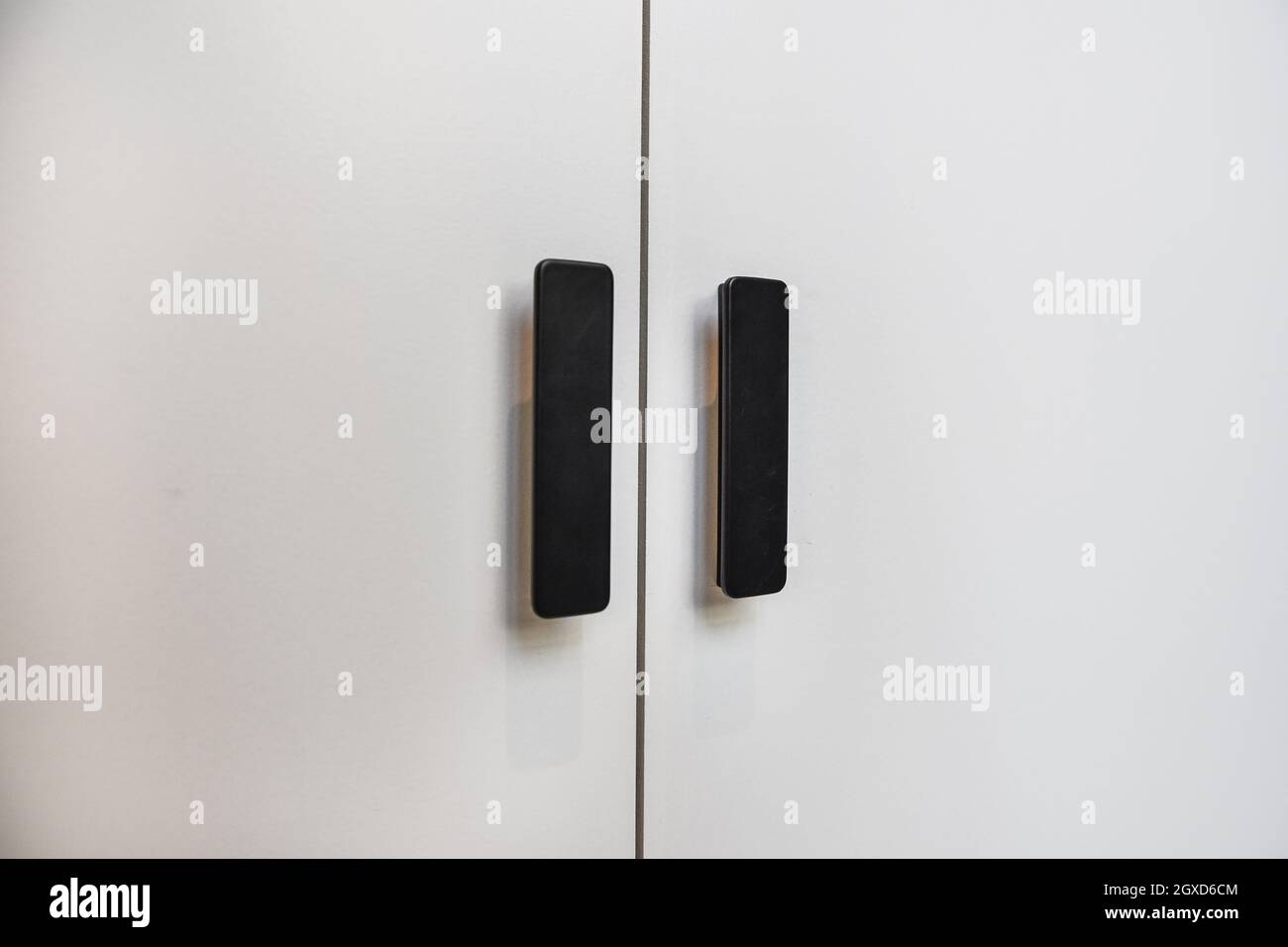 Maniglie nere rettangolari su porte luminose con superficie liscia e pulita in una casa moderna Foto Stock