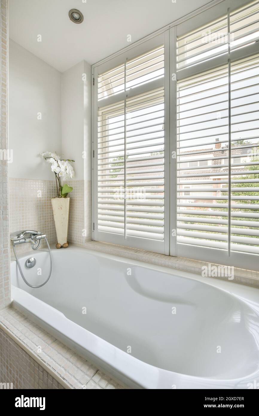 https://c8.alamy.com/compit/2gxd7er/vasca-da-bagno-bianca-posta-vicino-alla-finestra-in-un-elegante-bagno-con-pareti-piastrellate-beige-in-un-moderno-appartamento-di-giorno-2gxd7er.jpg
