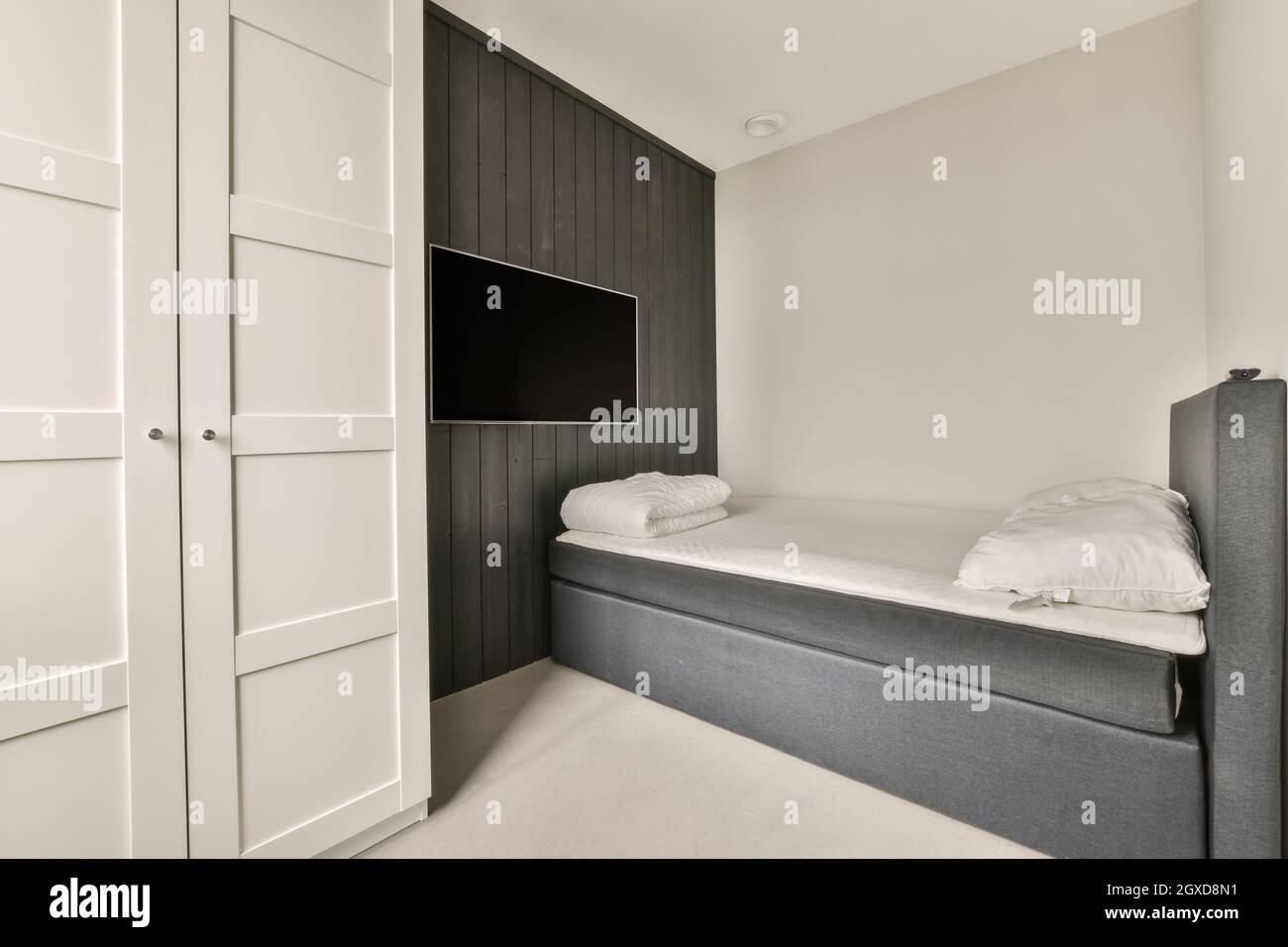 Letto con biancheria bianca e asciugamano posto vicino a TV con schermo nero in luminosa camera da letto in appartamento Foto Stock