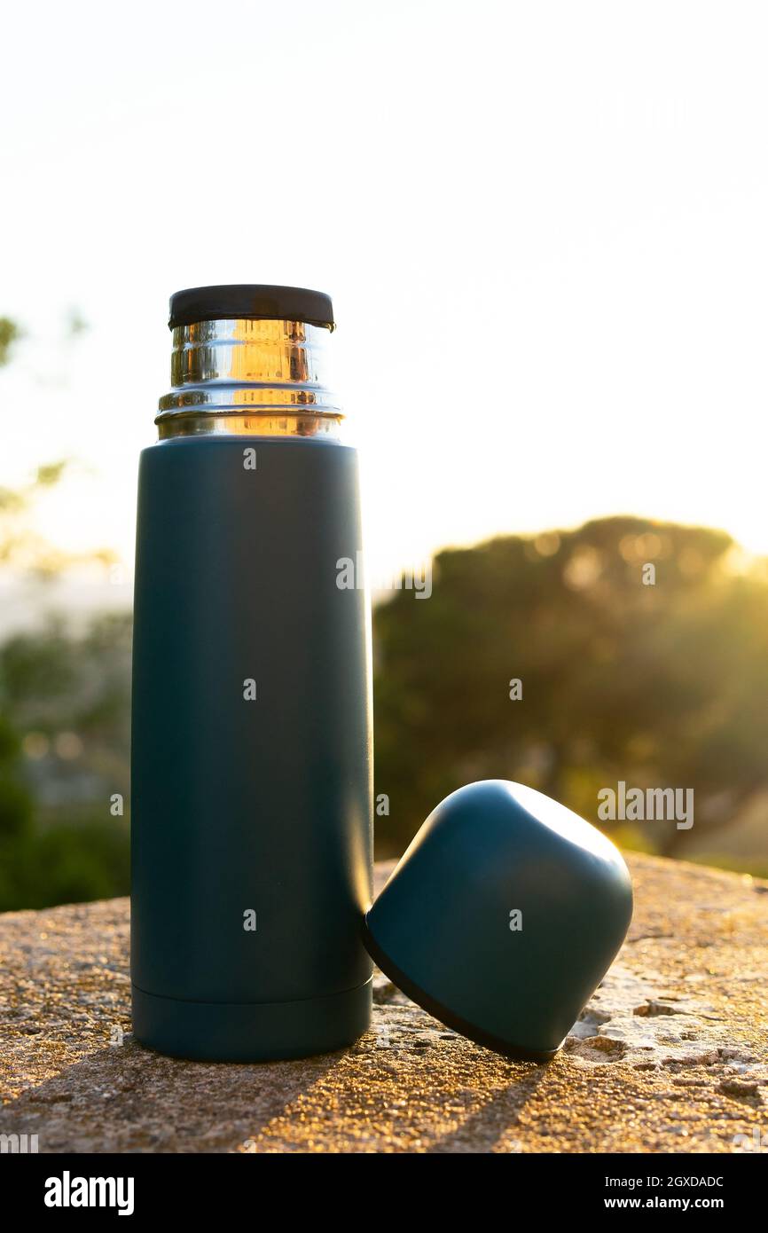 Moderni thermos in acciaio inox e plastica con coppa su superficie ruvida sotto il cielo lucido al tramonto Foto Stock