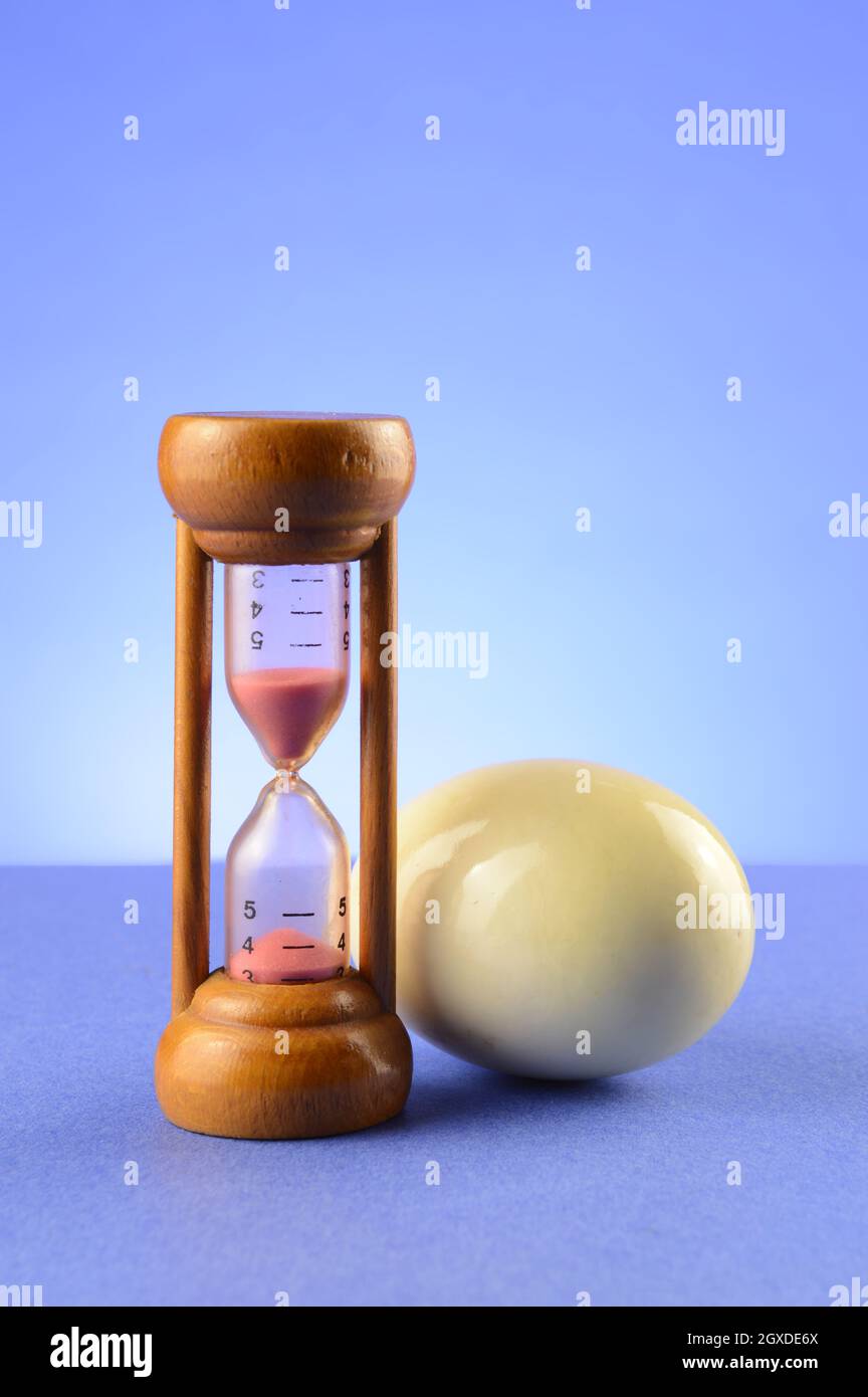 Un timer per le uova da cucina con un uovo sodo su sfondo blu. Foto Stock