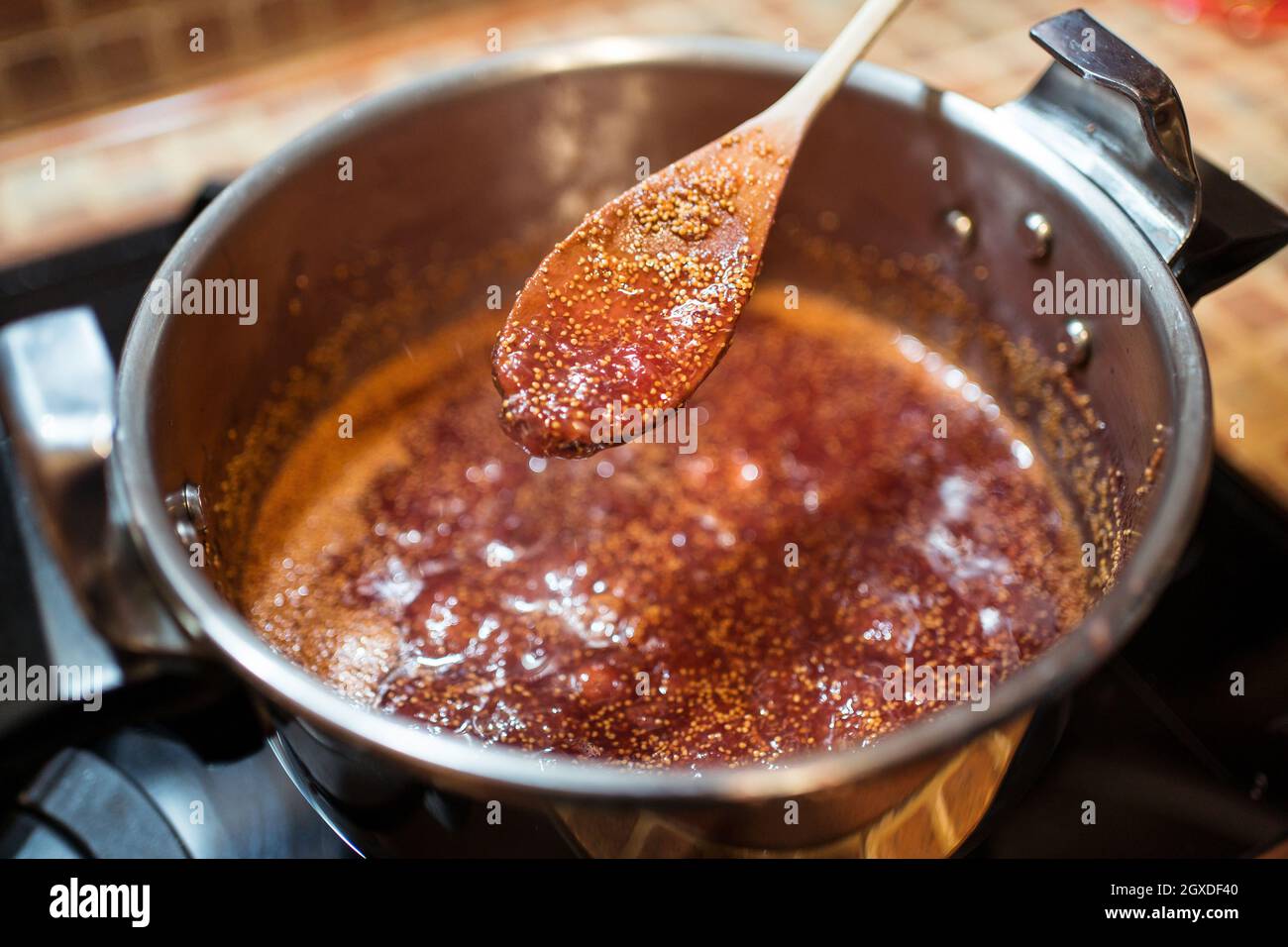 Da sopra di raccolto anonima persona mescolando confit di fichi in fornello su stufa a casa Foto Stock