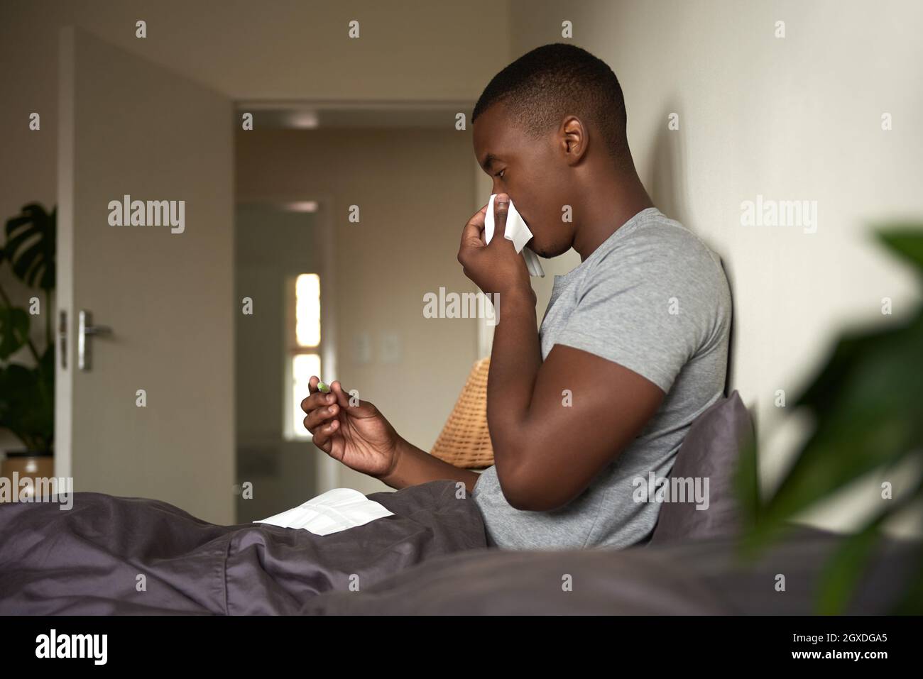 Giovane africano con un freddo che controlla la sua temperatura a letto Foto Stock