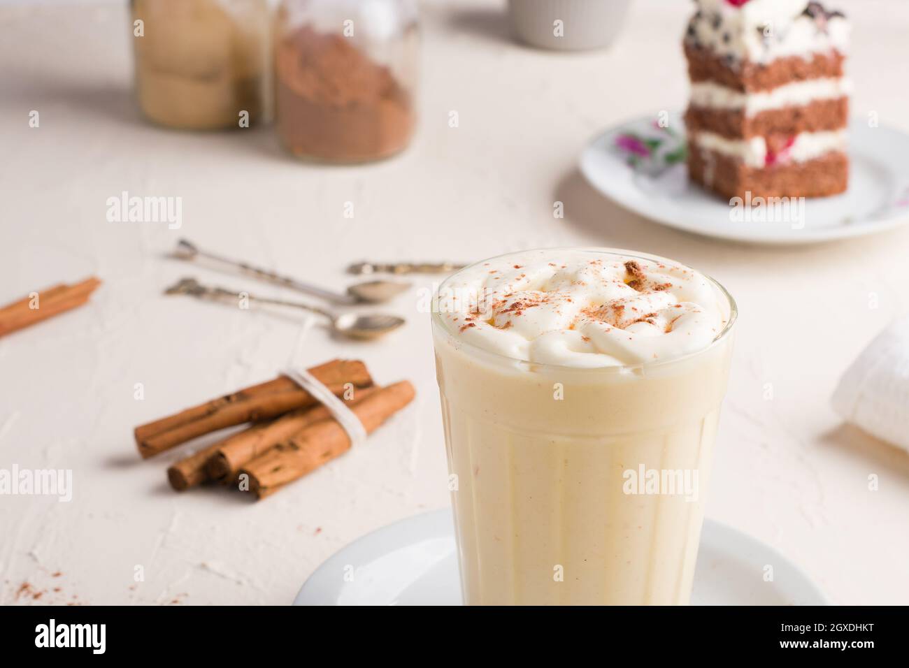 Bicchiere di punch al latte con polvere di cannella su uovo bianco montato  contro pezzo di torta sul tavolo della caffetteria su sfondo chiaro Foto  stock - Alamy