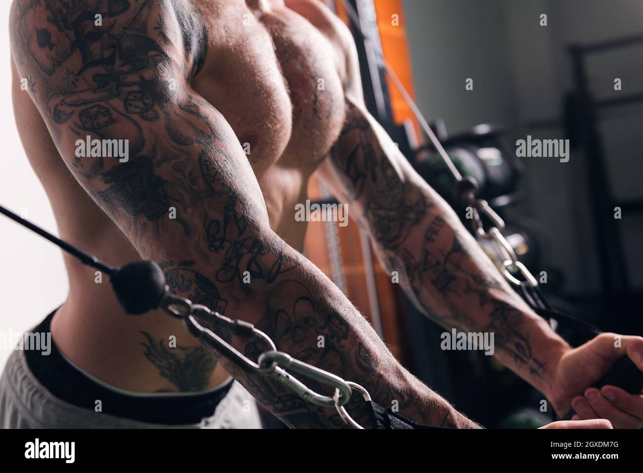 Vista laterale di raccolto concentrato sportivo muscolare con tatuaggi facendo esercizi su cavo crossover macchina in palestra con pareti leggere Foto Stock