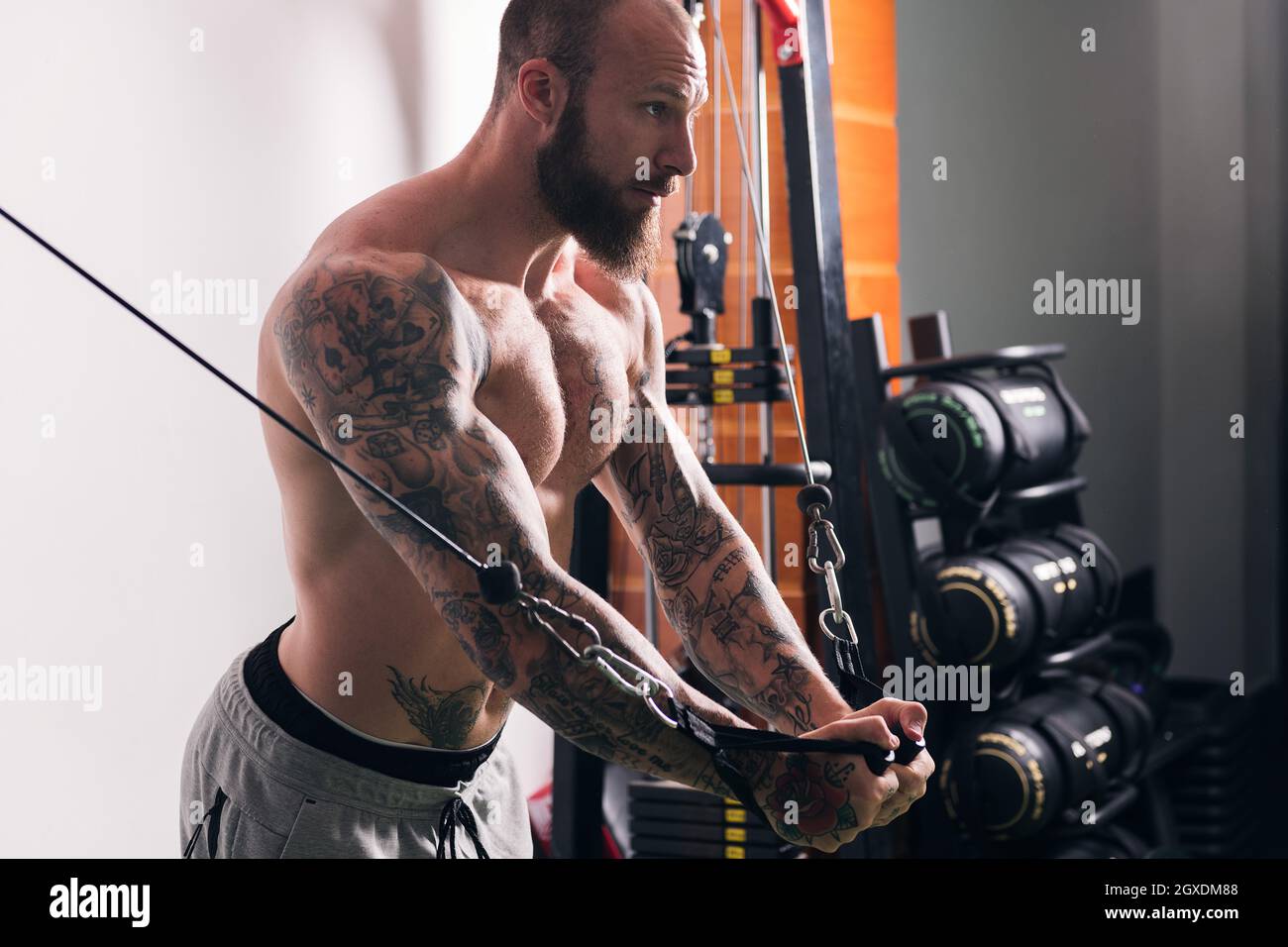 Vista laterale di raccolto concentrato sportivo muscolare con tatuaggi facendo esercizi su cavo crossover macchina in palestra con pareti leggere Foto Stock