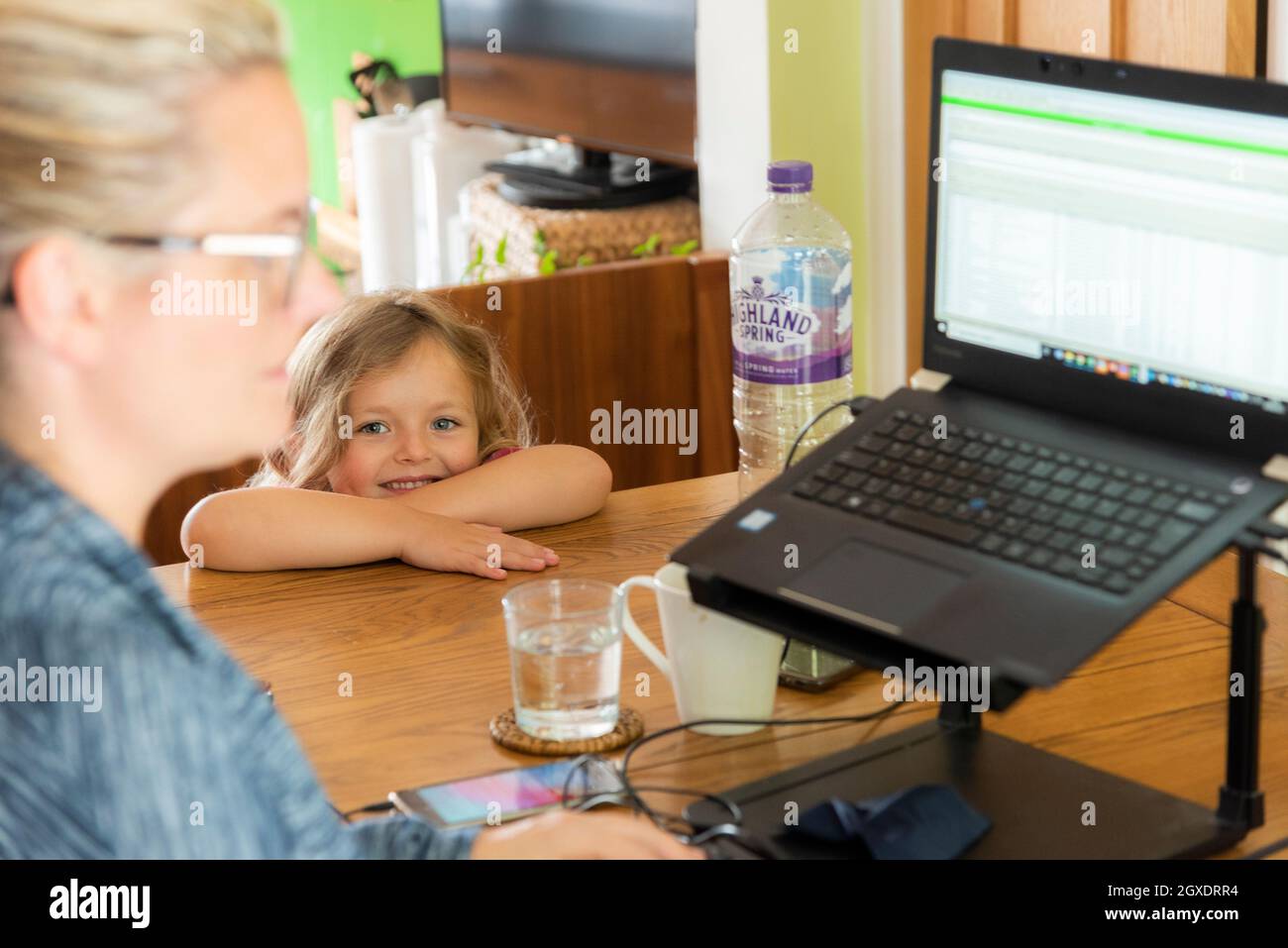 Una donna che lavora da casa durante la pandemia di Covid 19, con la sua figlia che guarda. Foto Stock
