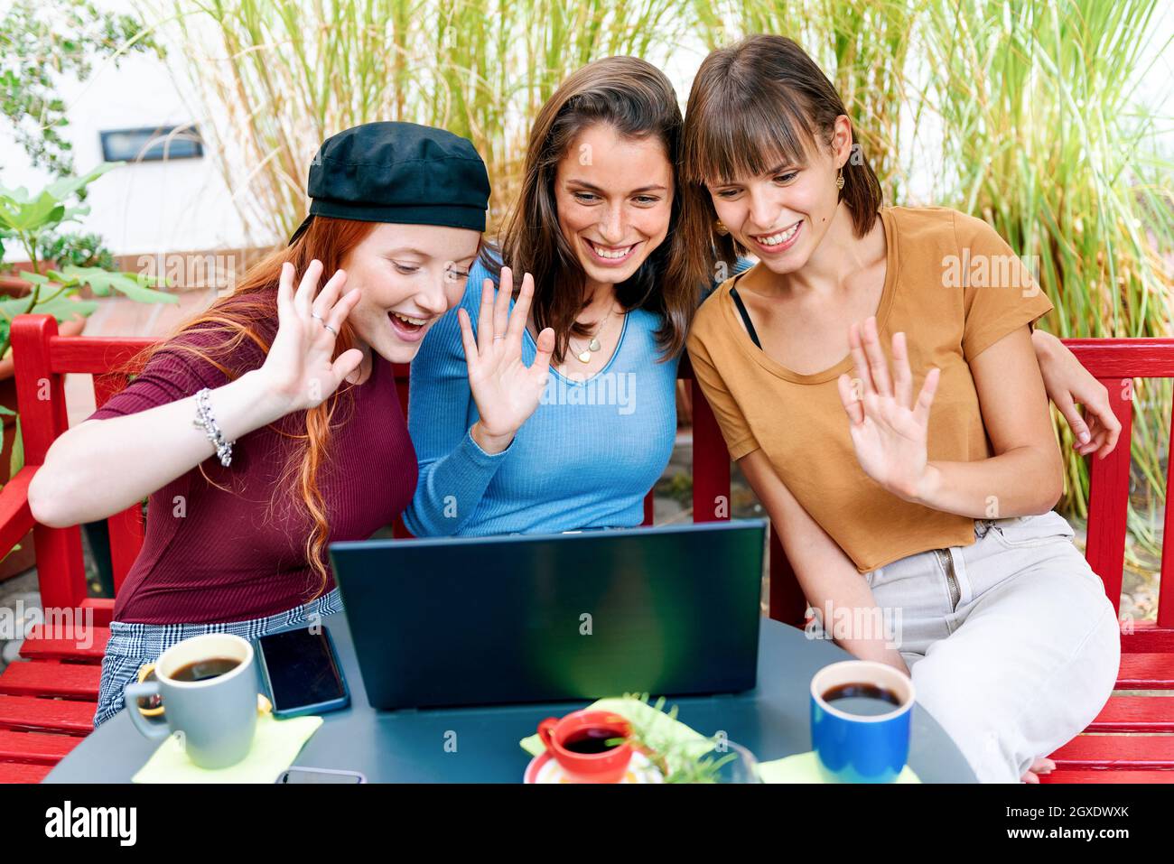 Tre sorridenti giovani donne felici che hanno una videochiamata su un computer portatile che sventolano in un saluto sullo schermo per la comunicazione a lunga distanza Foto Stock