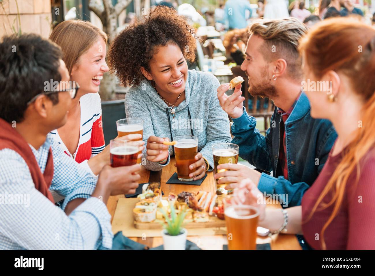 Gruppo di diversi amici multietnici che si divertono in un pub ridendo e scherzando su pinte di birra fredda con attenzione a una giovane donna nera attraente in Foto Stock