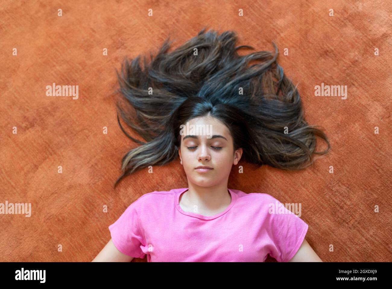 Da sopra di tranquilla adolescente femminile con lunghi capelli scuri distesi con occhi chiusi su pavimento arancione Foto Stock