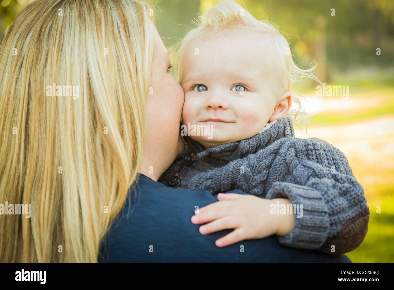 Madre che abbraccia il suo adorabile Bionda capelli Blue Eyed Baby Boy all'aperto. Foto Stock