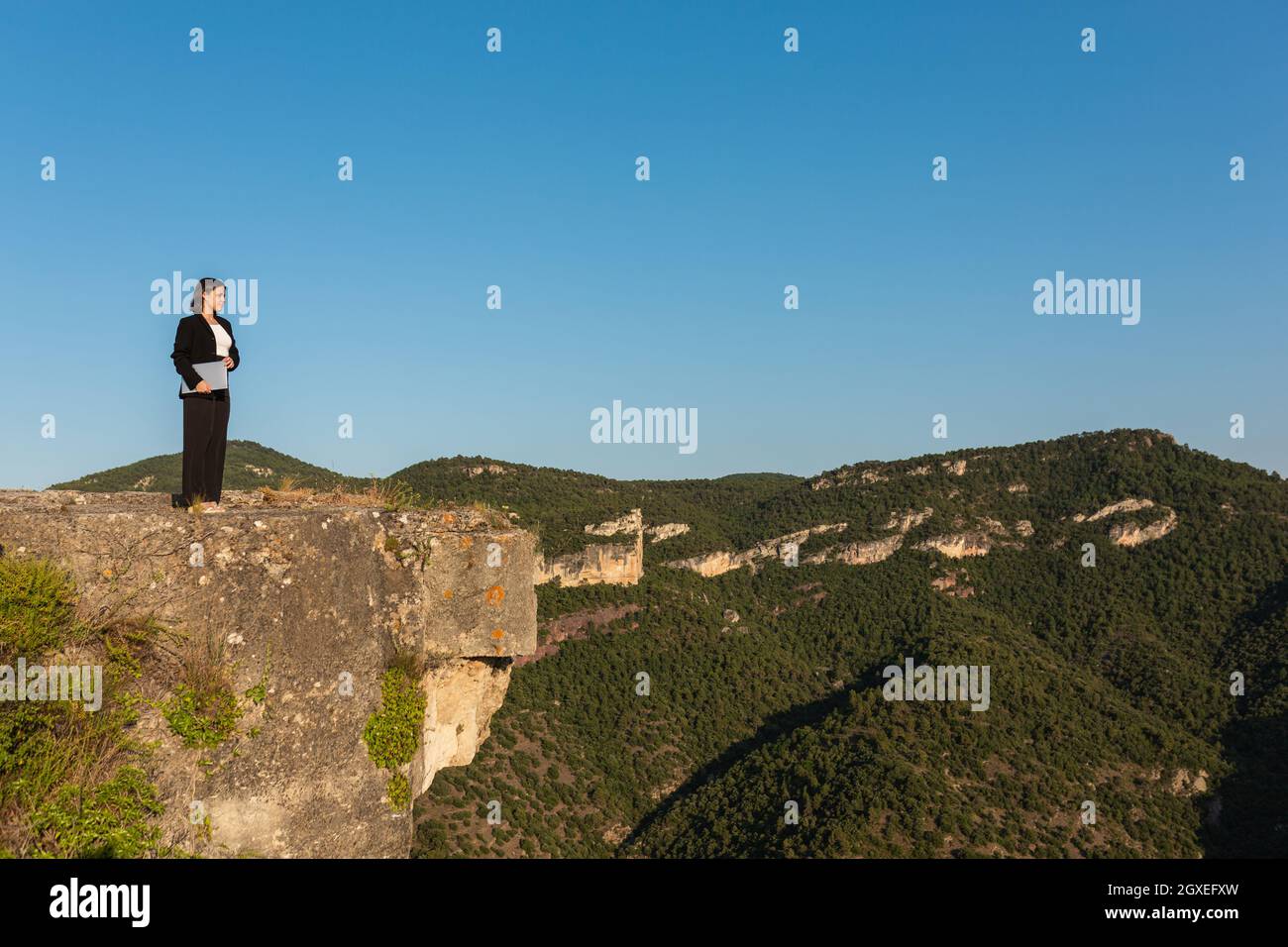 Donna d'affari sicura con un notebook in piedi su una cima rocciosa Foto Stock