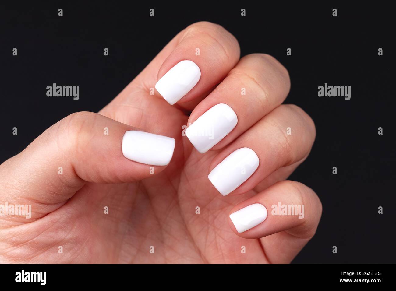 Mano femminile con bel manicure - chiodi bianchi su sfondo nero. Concetto di cura delle unghie Foto Stock