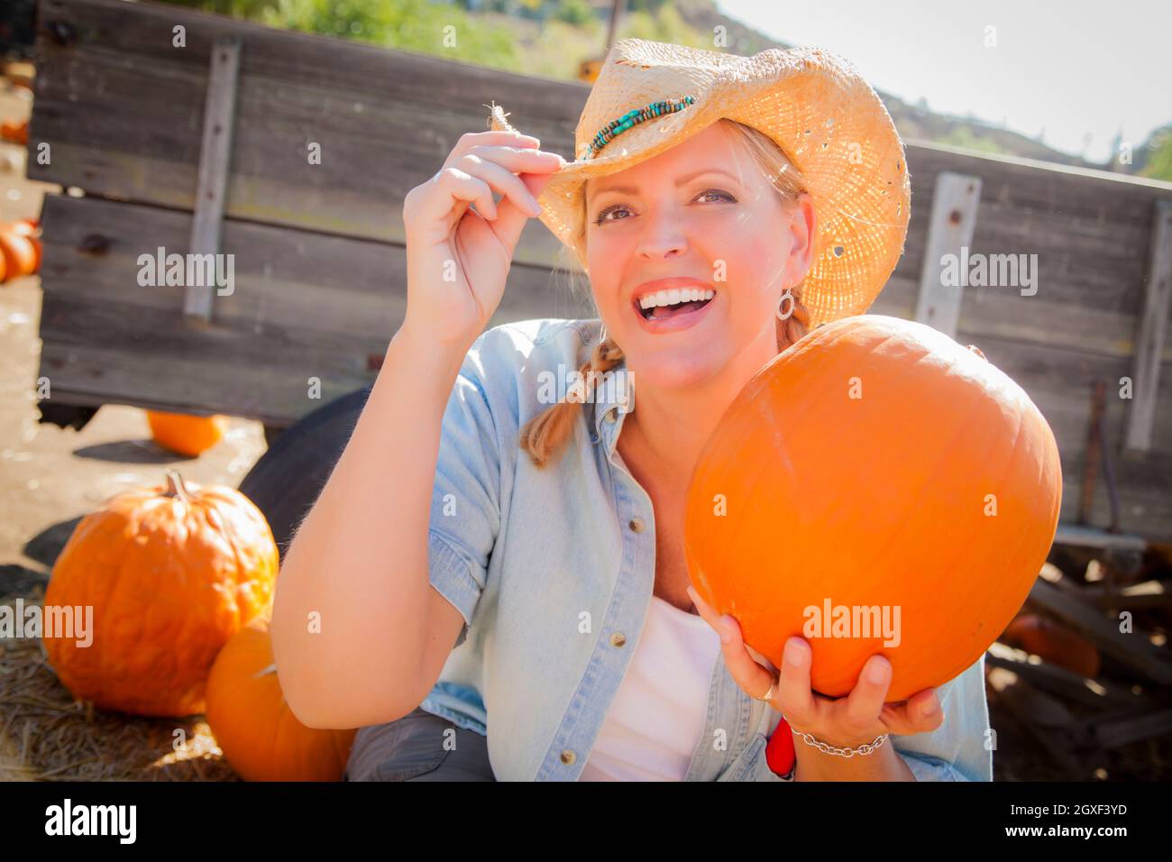 Bella Donna bionda Rancher indossando il cappello da cowboy detiene una zucca in un rustico di impostazione per il paese. Foto Stock