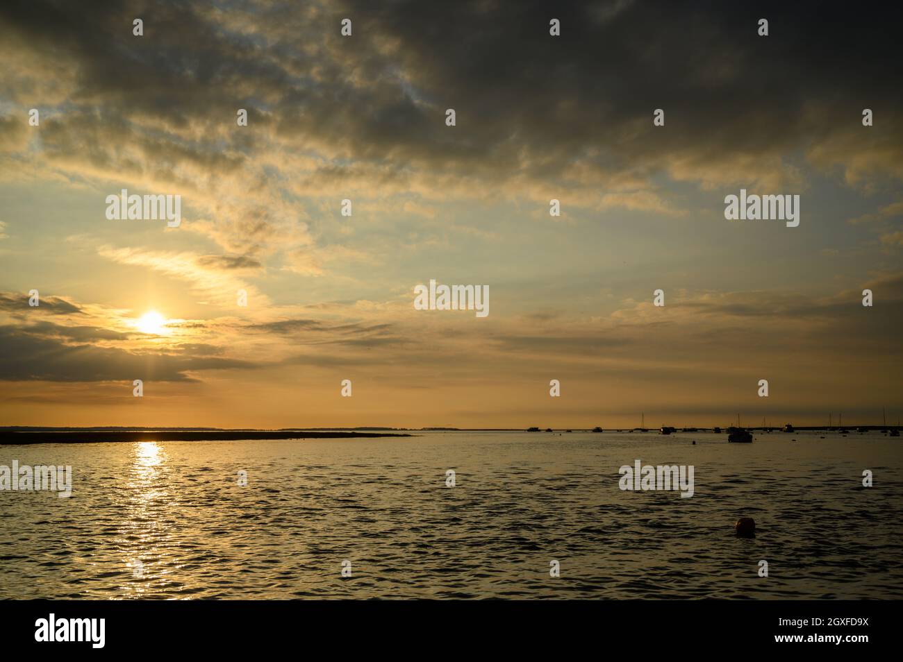 Cielo spettacolare con il sole che tramonta sulla costa del Mare del Nord vicino a Blakeney Point con barche in silhouette ormeggiate sull'acqua, Norfolk, Inghilterra. Foto Stock