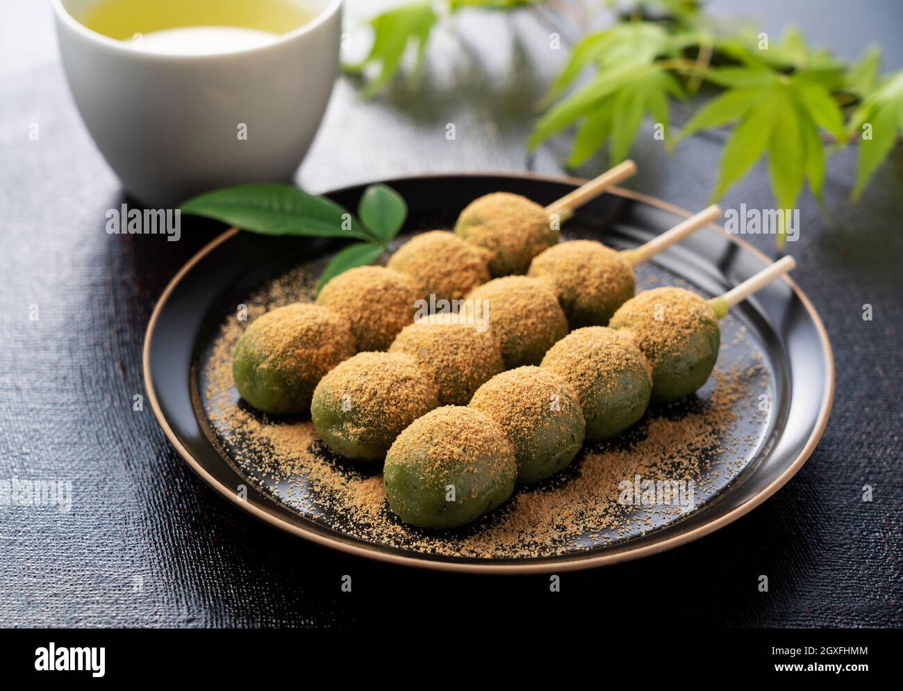 Gnocchi d'erba ricoperti di farina di soia e tè verde serviti su un piatto nero posto su sfondo nero. Gnocchi giapponesi. Foto Stock