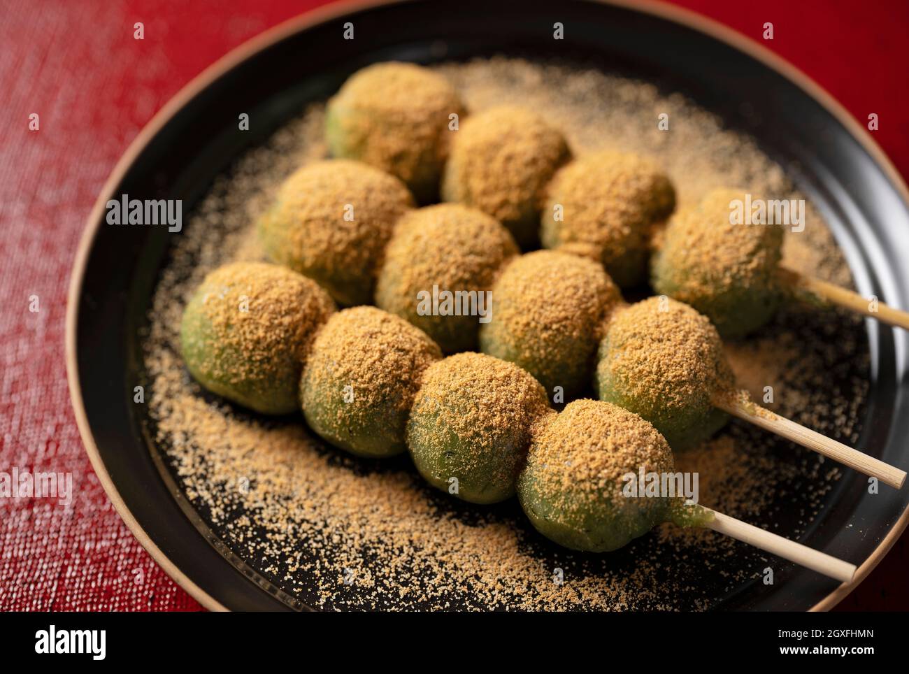 Gnocchi di mugwort ricoperti di farina di soia, serviti su un piatto nero posto su un vassoio rosso gnocchi giapponesi. Foto Stock