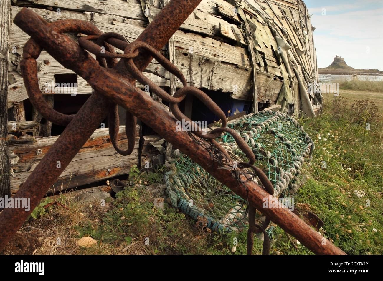 Vecchia ancora, scafo in legno e vaso di aragosta, con il 16 ° secolo Lindisfarne Castello in lontananza, Holy Island, Northumberland, Regno Unito. Foto Stock