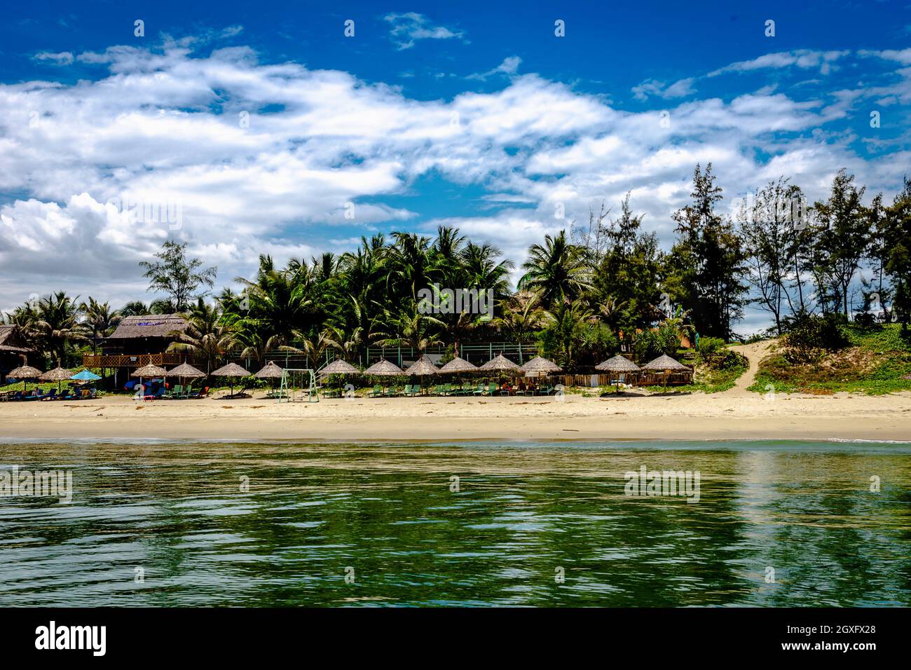 Una spiaggia bang dall'acqua guardando le sedie a sdraio e capanne coperte di paglia. Foto Stock