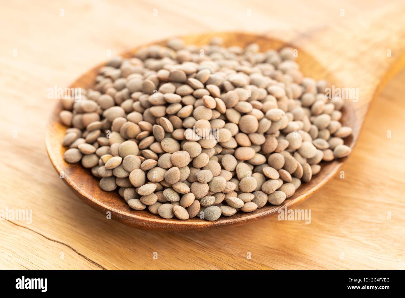 Lenticchie su cucchiaio di legno su tavolo. Lente variabilis Foto Stock