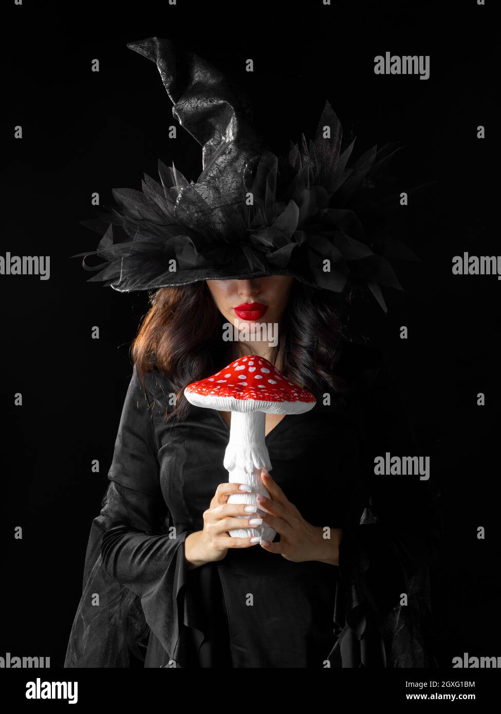 Ritratto di strega strega strega donna in costume di Halloween che tiene fungo velenoso per pozione isolato su sfondo nero Foto Stock