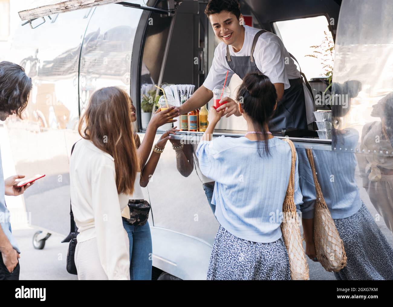 Un addetto alle vendite sorridente che offre bevande ai clienti mentre si trova in un veicolo alimentare Foto Stock