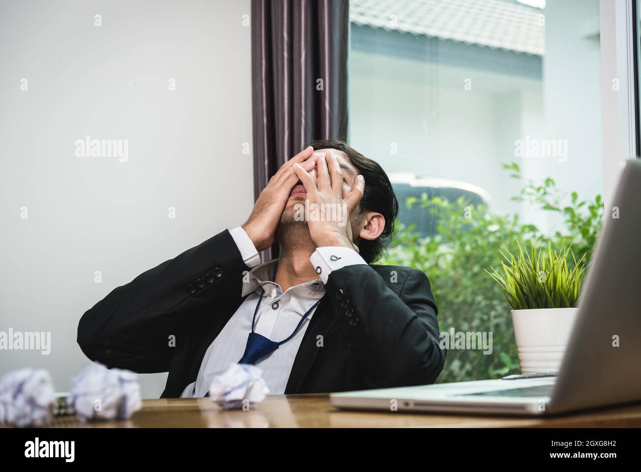 Un uomo d'affari seduto sulla scrivania è preoccupato per la fatica di casa ufficio Foto Stock Un uomo d'affari seduto sulla scrivania è preoccupato per la fatica di casa ufficio Foto Stock