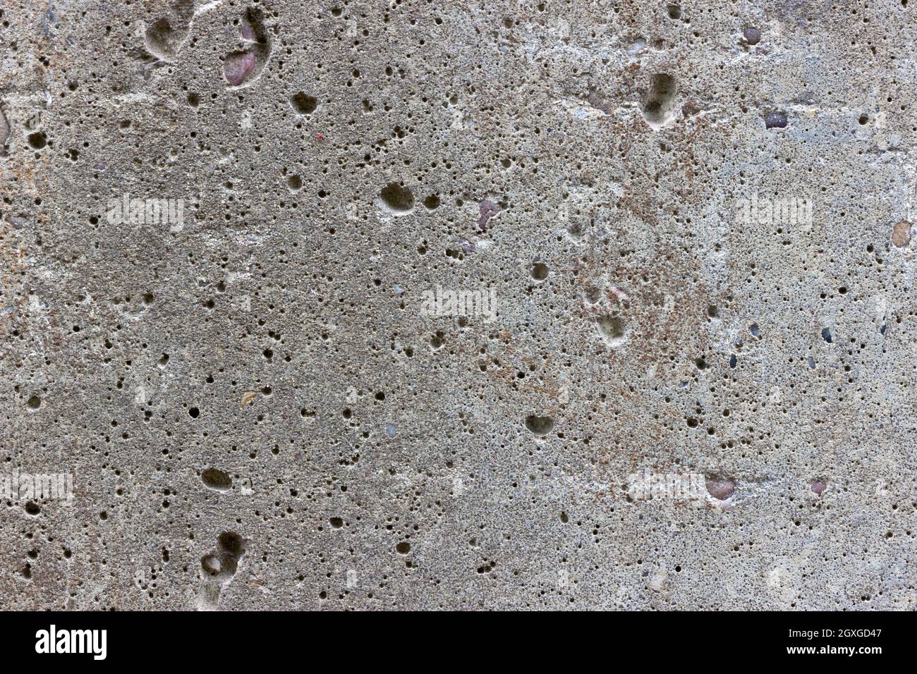 Una superficie piana in cemento grigio. La superficie è testurizzata e coperta da fori di molte piccole bolle d'aria. Foto Stock