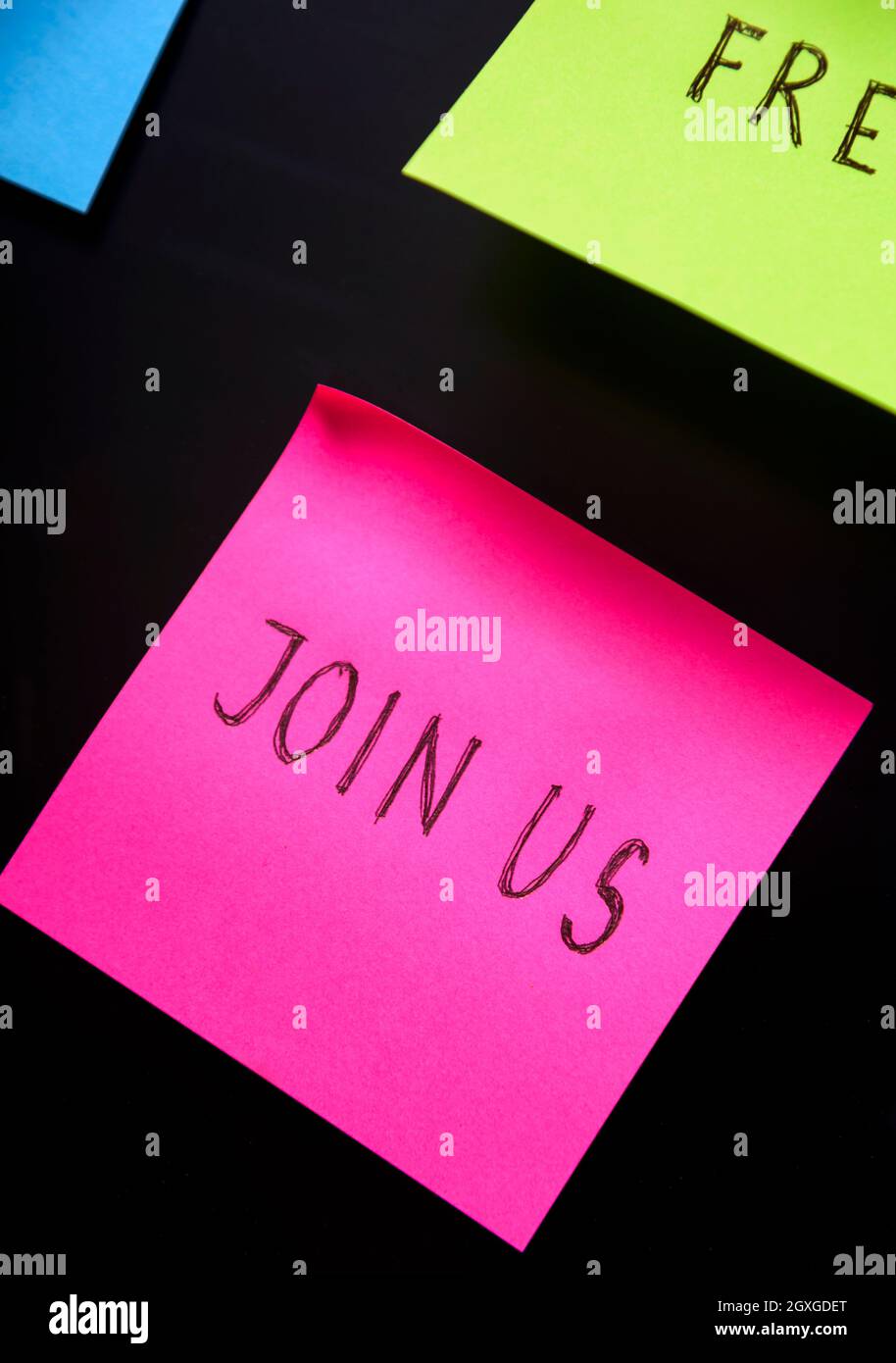 Unisciti a noi scritto e accedi adesivo su pineboard. Note colorate adesive sullo sfondo della lavagna nera. Unitevi a noi e partecipate al nostro team business c Foto Stock