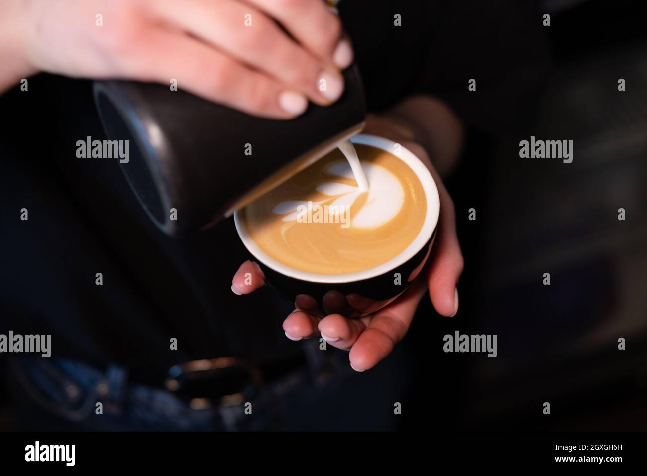 Barista che versa la schiuma di latte su caffè, espresso. Per creare un latte art perfetto, colori scuri, caffetteria. Foto Stock
