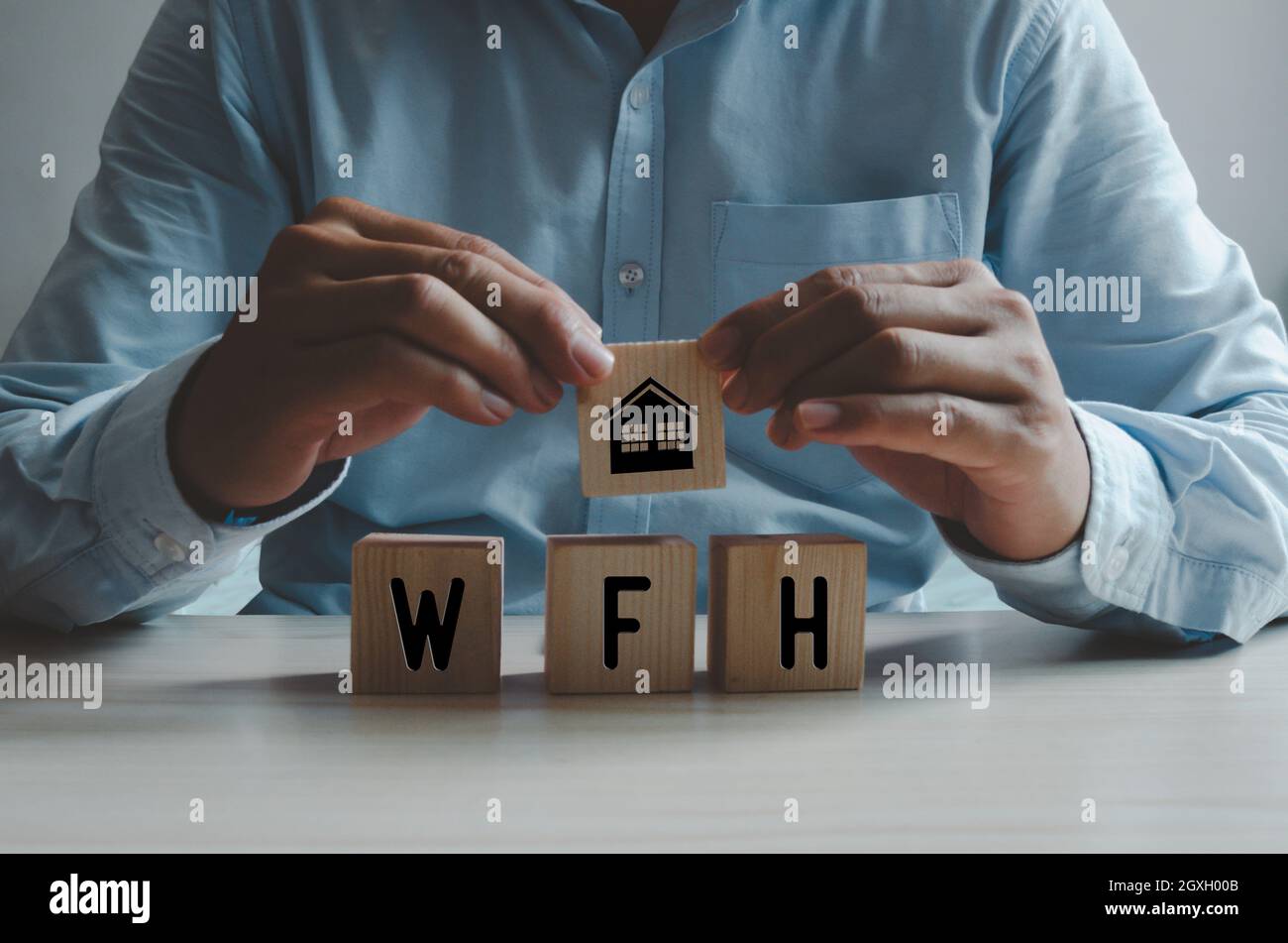 Lavoro dal concetto domestico di affari. Mano dell'uomo che tiene un cubo di legno con un'icona della casa. Foto Stock