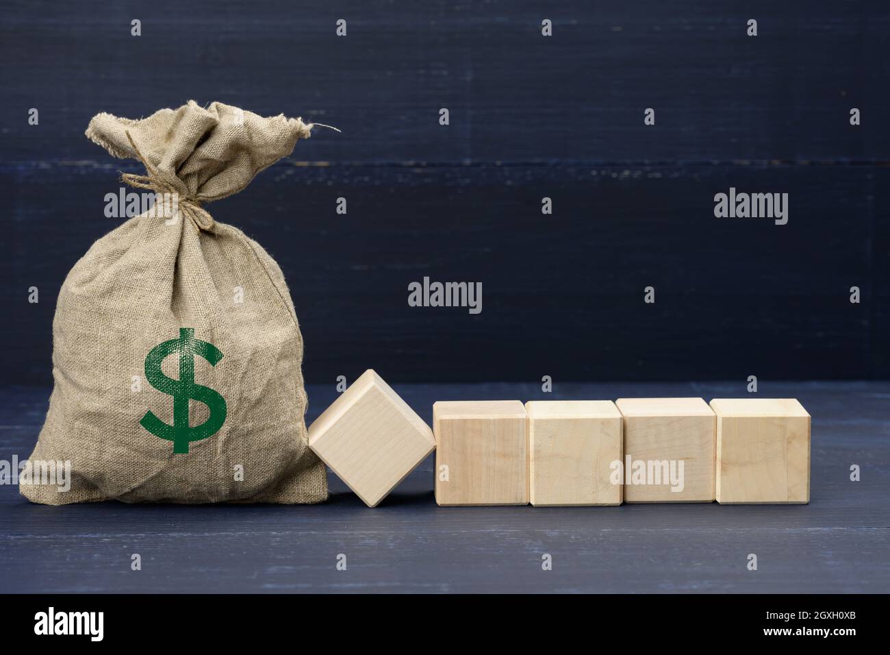 Borsa di tela marrone completa con icona del dollaro USA e cinque cubetti bianchi di legno su sfondo blu. Ricchezza, investimenti, sussidi e concetto di risparmio, luogo per Foto Stock