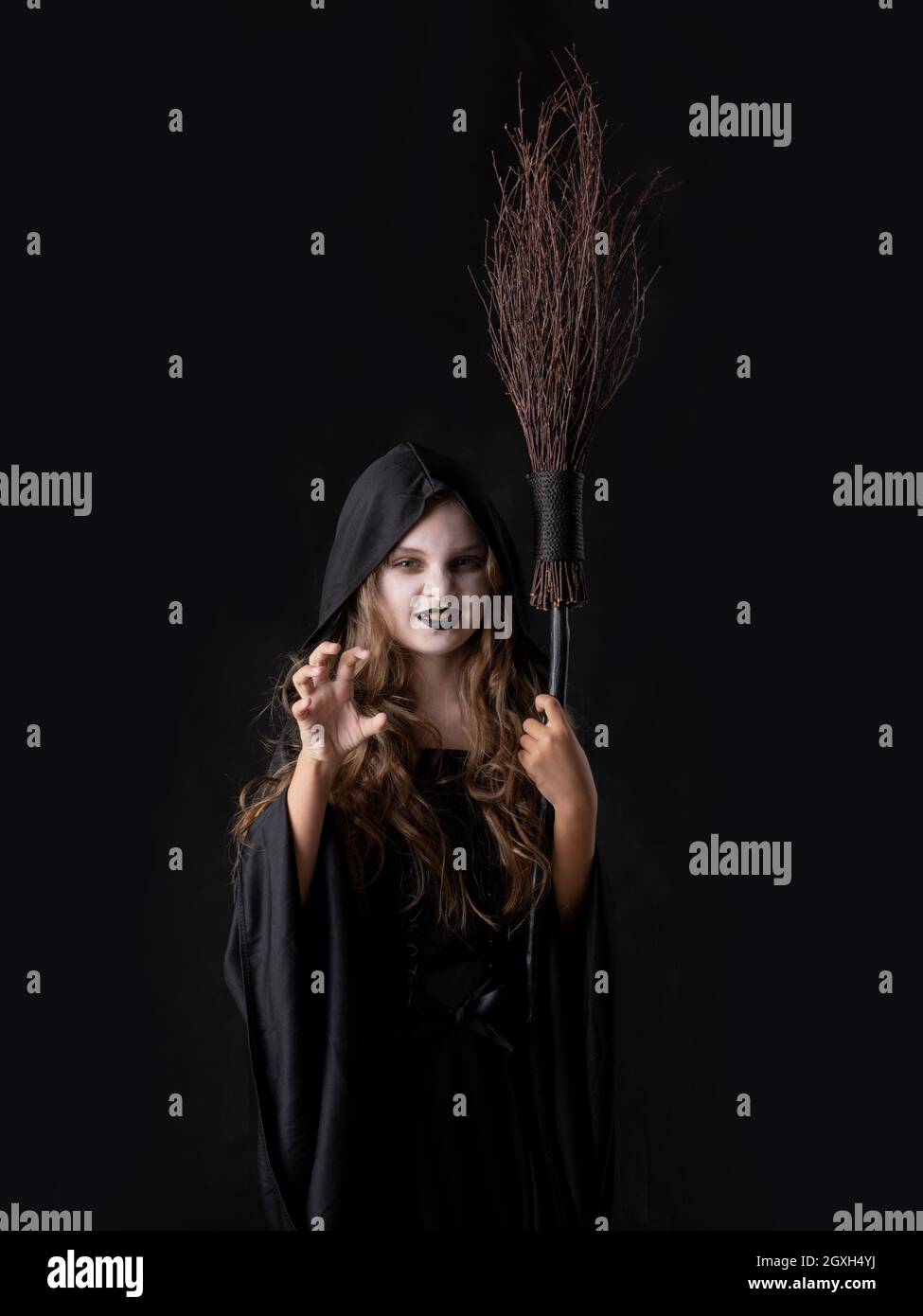 Ragazza in Halloween male arrabbiato strega costume grin snarl tenere scopa isolato su sfondo nero Foto Stock
