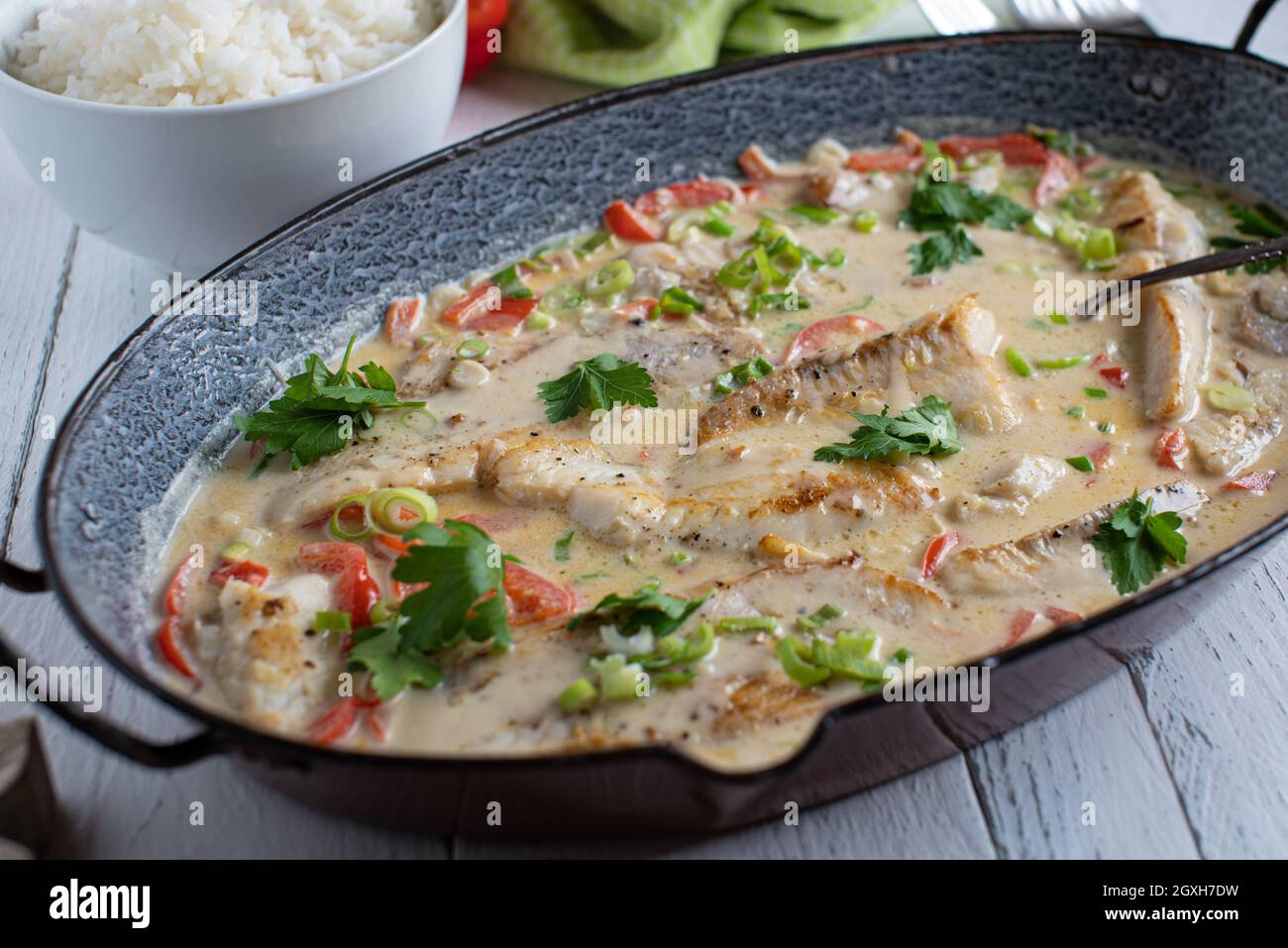 Piatto di pesce con filetto di scorfano fritto cotto in un delizioso latte di cocco con verdure. Servito in una casseruola rustica piatto su tavola di legno dall'alto Foto Stock