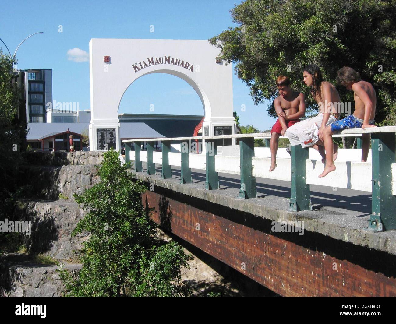 Tre tuffatori di penny siedono sul binario del ponte all'entrata del Villaggio di Whaka a Rotorua, Nuova Zelanda. Whaka Village è un villaggio termale dove vivono i residenti e turisti visitare. I tuffatori del penny sono bambini che attendono al ponte d'ingresso per i visitatori di gettare le monete nel torrente Puarenga sotto dove i bambini si tufferanno per loro. Questa consuetudine è in corso da decenni. Foto Stock