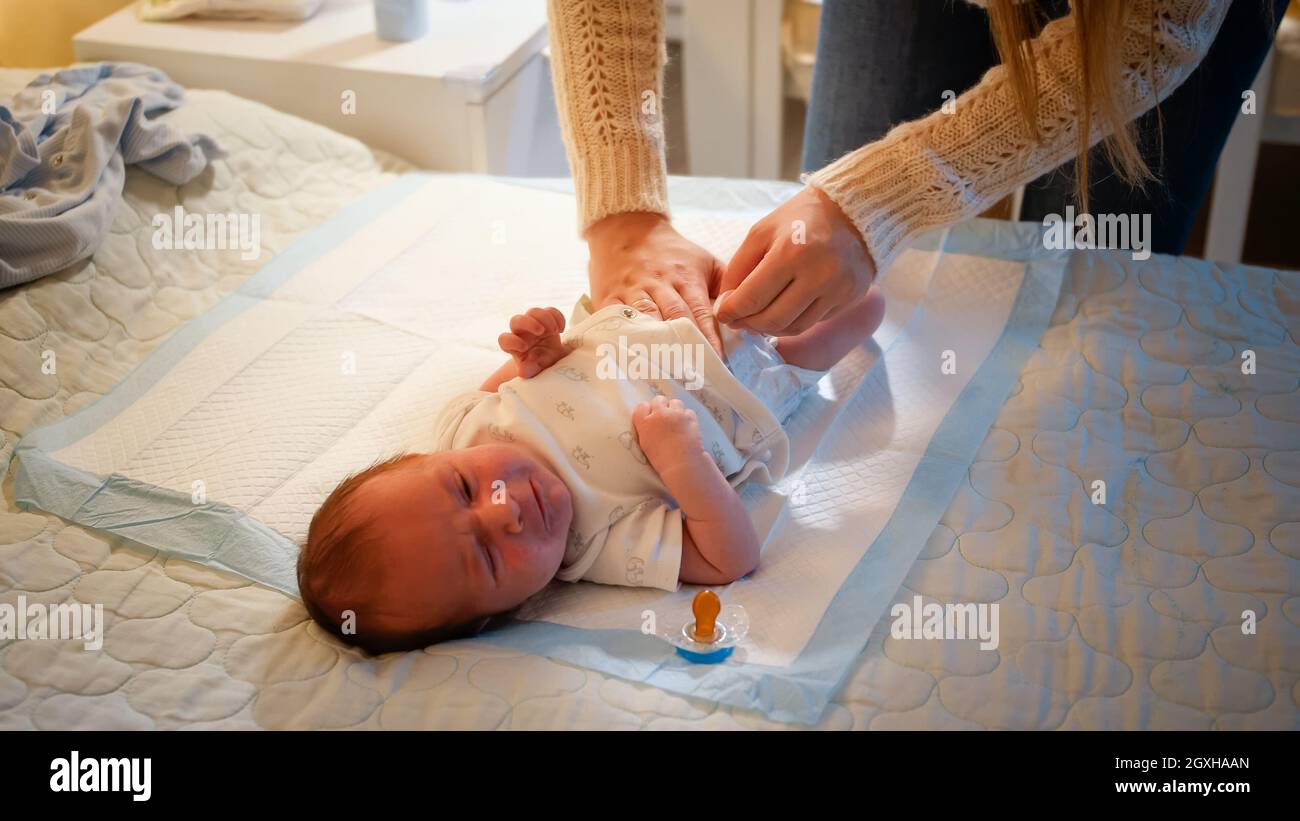 Giovane madre che cambia i pannolini sudicio al suo bambino neonato che  piange a letto di