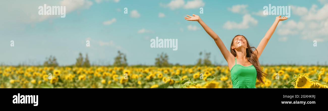 Primavera felice donna con braccia aperte a piedi in campo di girasole godendo libero paesaggio naturale banner panoramico. Ragazza asiatica rilassante respirando aria pulita Foto Stock