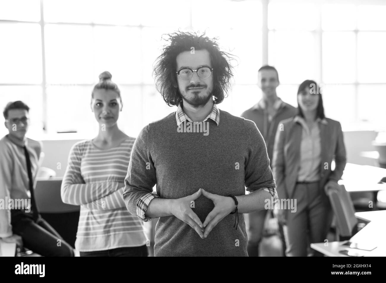 Ritratto di giovane sorridente casuall imprenditore con i colleghi in background in ufficio Foto Stock