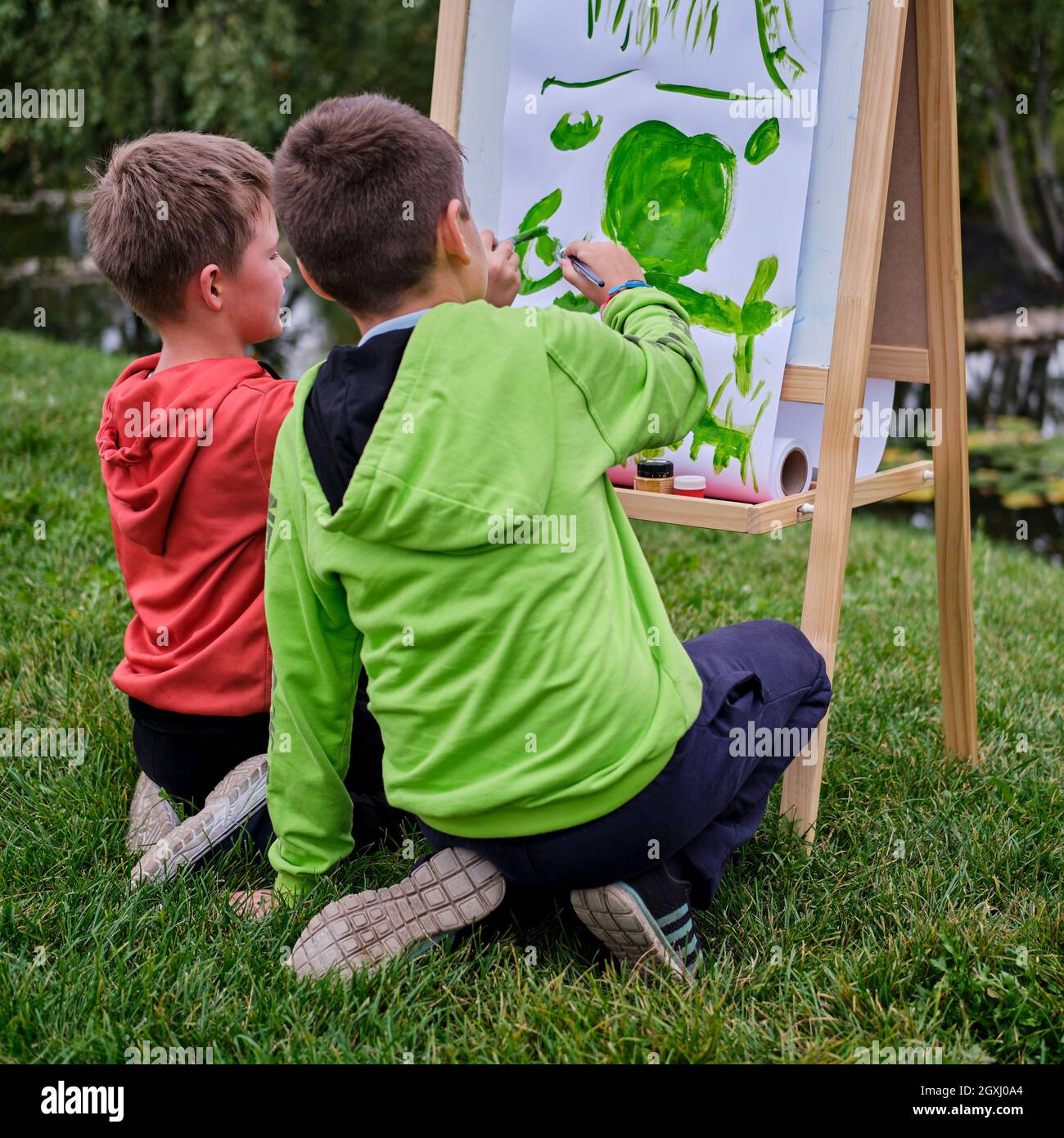 I bambini imparano a dipingere su tela, a cavalletto con carta. Ragazzo  artista dipinge la natura e gli alberi dalla superficie d'acqua del fiume  Foto stock - Alamy