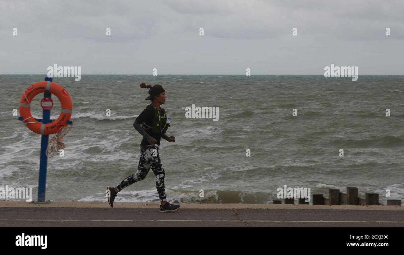 Donna in leggings lunghi che fa jogging sul lungomare in una giornata ventosa d'autunno. Mare agitato e cielo grigio sullo sfondo. Foto Stock