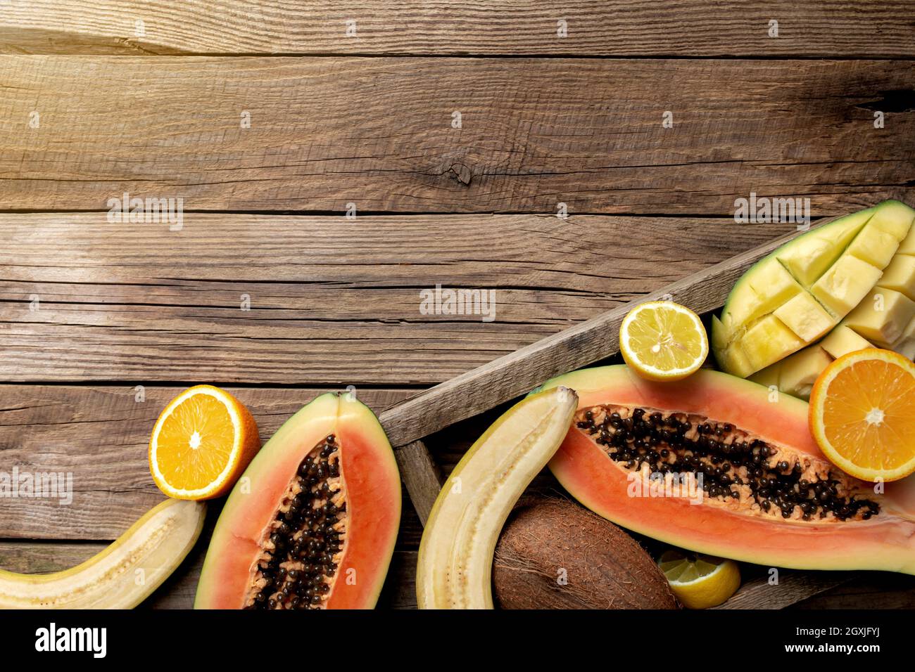 Frutta tropicale fresca in una scatola di consegna di legno su sfondo di legno. Papaya, arancio, banana, cocco, mango e limone vista dall'alto piatto con copia sp Foto Stock