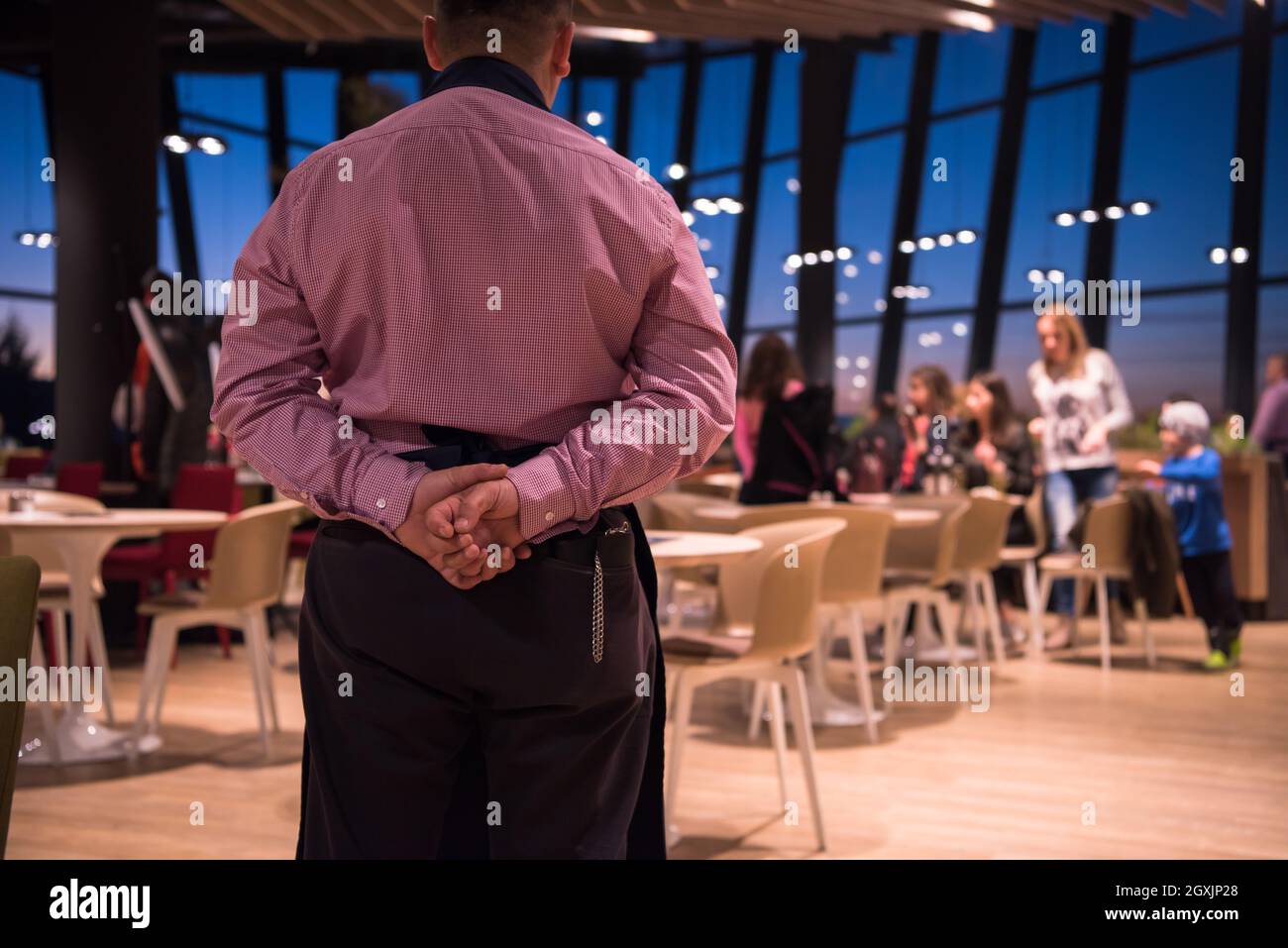 Vista posteriore del giovane cameriere fiducioso in piedi con le mani dietro la schiena in un ristorante di lusso Foto Stock